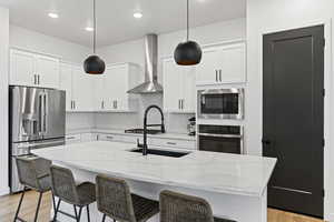 Kitchen featuring wall chimney range hood, light wood-style flooring, decorative backsplash, and appliances with stainless steel finishes