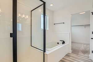 Full bathroom with a shower stall, wood finished floors, a spacious closet, a bath, and baseboards