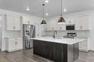 Kitchen with dark wood-style flooring, hanging light fixtures, appliances with stainless steel finishes, a sink, and decorative backsplash