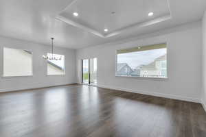 Interior space with baseboards, dark wood-type flooring, a textured ceiling, a tray ceiling, and a chandelier