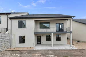 Back of property featuring a shingled roof, stucco siding, a patio area, and a balcony