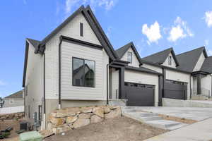 View of front of property featuring concrete driveway, brick siding, central AC, and a garage