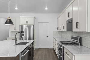 Kitchen with dark wood-style flooring, a sink, stainless steel appliances, backsplash, and pendant lighting