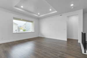 Spare room with visible vents, baseboards, dark wood-style floors, a tray ceiling, and recessed lighting