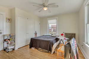 Unit 6 - Bedroom featuring radiator heating unit, a ceiling fan, and wood finished floors