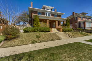 American foursquare style home featuring brick siding, a front yard, stairway, and a chimney