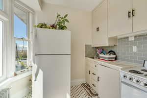 Unit 6 - Kitchen with light countertops, radiator, tasteful backsplash, white appliances, and white cabinets