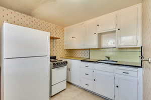 Kitchen featuring white cabinetry, white appliances, backsplash, a sink, and tile countertops