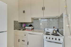 Unit 6 - Kitchen featuring white appliances, light countertops, decorative backsplash, and a sink