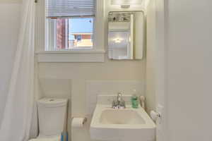 Unit 6 - Bathroom featuring a shower with shower curtain, toilet, decorative backsplash, and a sink