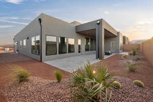 Back of house at dusk with a patio area, a fenced backyard, and stucco siding