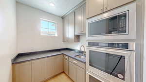 Kitchen featuring a textured ceiling, light wood-style flooring, dark countertops, appliances with stainless steel finishes, and a sink