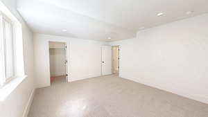 Unfurnished bedroom with a walk in closet, baseboards, light colored carpet, and recessed lighting