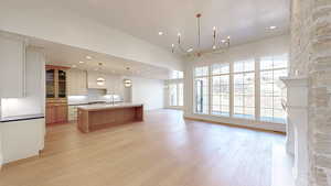 Kitchen featuring open floor plan, light wood-type flooring, an inviting chandelier, decorative backsplash, and a sink