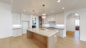 Kitchen featuring a center island with sink, arched walkways, a sink, light wood-style floors, and custom range hood