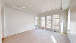 Empty room featuring a raised ceiling, arched walkways, baseboards, and light carpet