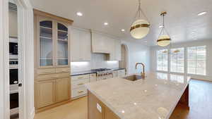 Kitchen with appliances with stainless steel finishes, light wood-type flooring, custom exhaust hood, and a sink