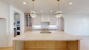 Kitchen featuring custom exhaust hood, arched walkways, a sink, a large island with sink, and backsplash