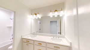 Bathroom with double vanity, a textured ceiling, a sink, and washtub / shower combination