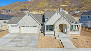 View of front facade with concrete driveway, stone siding, covered porch, a garage, and a chimney