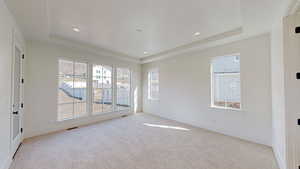Carpeted spare room with a textured ceiling, visible vents, and a raised ceiling