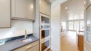 Kitchen featuring an inviting chandelier, dark stone countertops, a sink, light wood-style floors, and appliances with stainless steel finishes