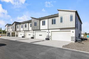 Townhome / multi-family property with concrete driveway, stone siding, board and batten siding, a residential view, and a garage