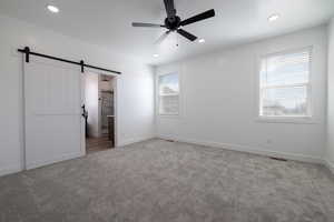Unfurnished bedroom with visible vents, baseboards, carpet, and a barn door