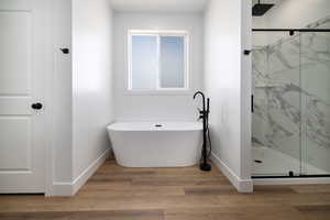 Bathroom with wood finished floors, a marble finish shower, baseboards, and a freestanding tub