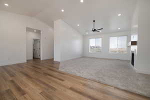 Unfurnished living room featuring a fireplace, light wood-type flooring, a ceiling fan, lofted ceiling, and baseboards