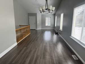 Unfurnished dining area featuring vaulted ceiling, baseboards, a chandelier, dark wood-style floors, and visible vents