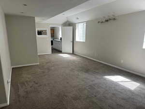Carpeted empty room with a sink, baseboards, lofted ceiling, and visible vents
