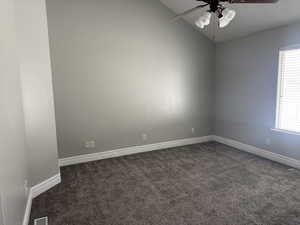 Spare room with baseboards, lofted ceiling, dark colored carpet, and ceiling fan