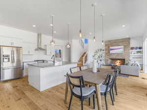 Kitchen with a fireplace, wall chimney range hood, stainless steel fridge, and light wood finished floors