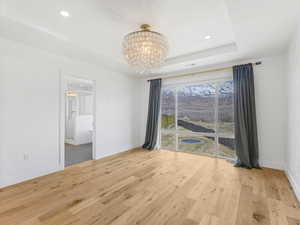 Empty room with baseboards, light wood-type flooring, an inviting chandelier, and a raised ceiling