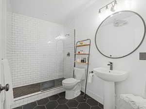 Full bathroom with tile patterned flooring, a tile shower, toilet, baseboards, and a sink