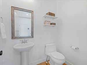 Half bathroom with baseboards, wood finished floors, toilet, and a sink