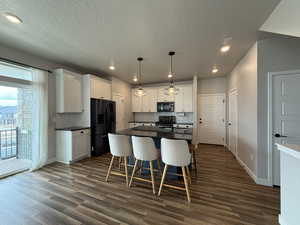Kitchen with white cabinets, a kitchen breakfast bar, dark wood finished floors, dark countertops, and black appliances