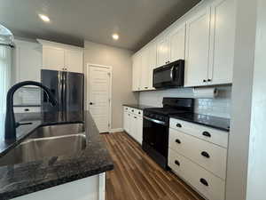 Kitchen featuring fridge with ice dispenser, dark wood-style flooring, range with gas stovetop, a sink, and black microwave