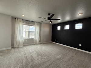 Carpeted spare room with a textured ceiling, baseboards, and ceiling fan