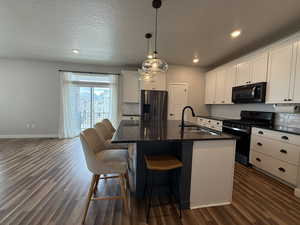 Kitchen with a sink, black microwave, gas range oven, stainless steel refrigerator with ice dispenser, and dark wood-style flooring