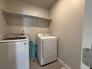Clothes washing area with light tile patterned flooring, washing machine and dryer, baseboards, and laundry area