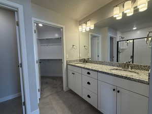 Full bathroom featuring double vanity, a sink, a walk in closet, and a shower stall