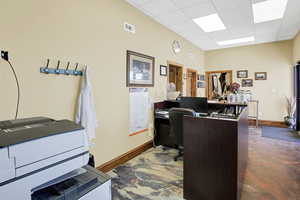 Office area with a paneled ceiling, concrete floors, visible vents, and baseboards