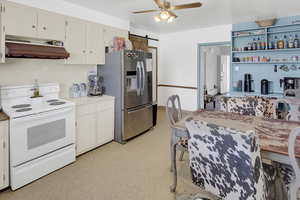 Kitchen with white electric stove, a barn door, under cabinet range hood, light floors, and stainless steel fridge