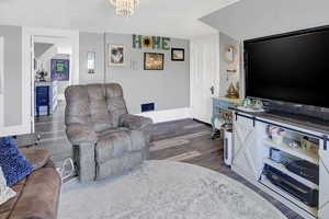 Living room with dark wood-type flooring, an inviting chandelier, and baseboards