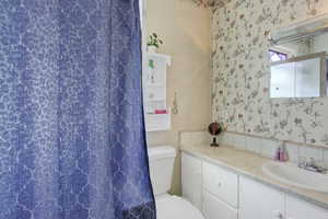 Bathroom with walk in shower, vanity, toilet, and wallpapered walls