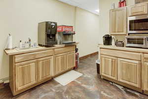 Kitchen featuring baseboards, stainless steel microwave, light brown cabinetry, a paneled ceiling, and a sink