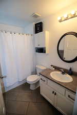 Bathroom with shower / bath combo, visible vents, toilet, tile patterned floors, and vanity