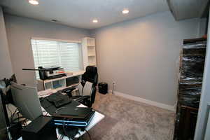 Carpeted home office featuring baseboards, visible vents, and recessed lighting